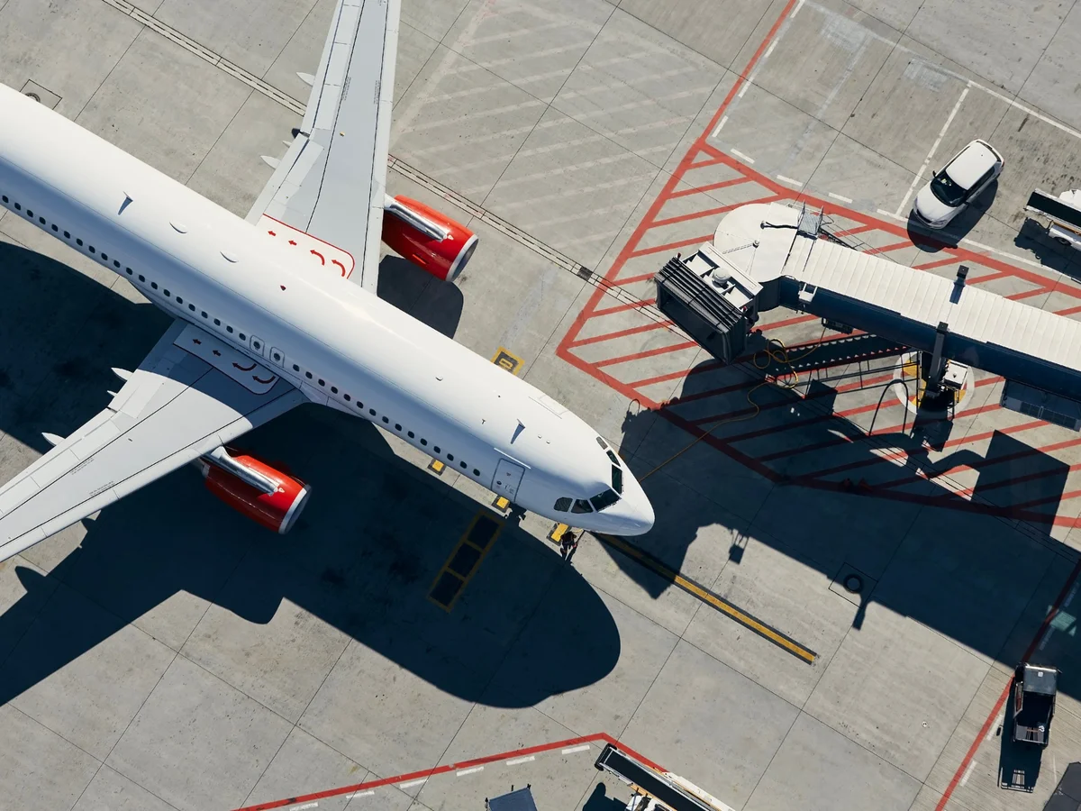 Aereo di linea al gate visto dall’alto, con pontile d’imbarco e mezzi di rampa sul piazzale