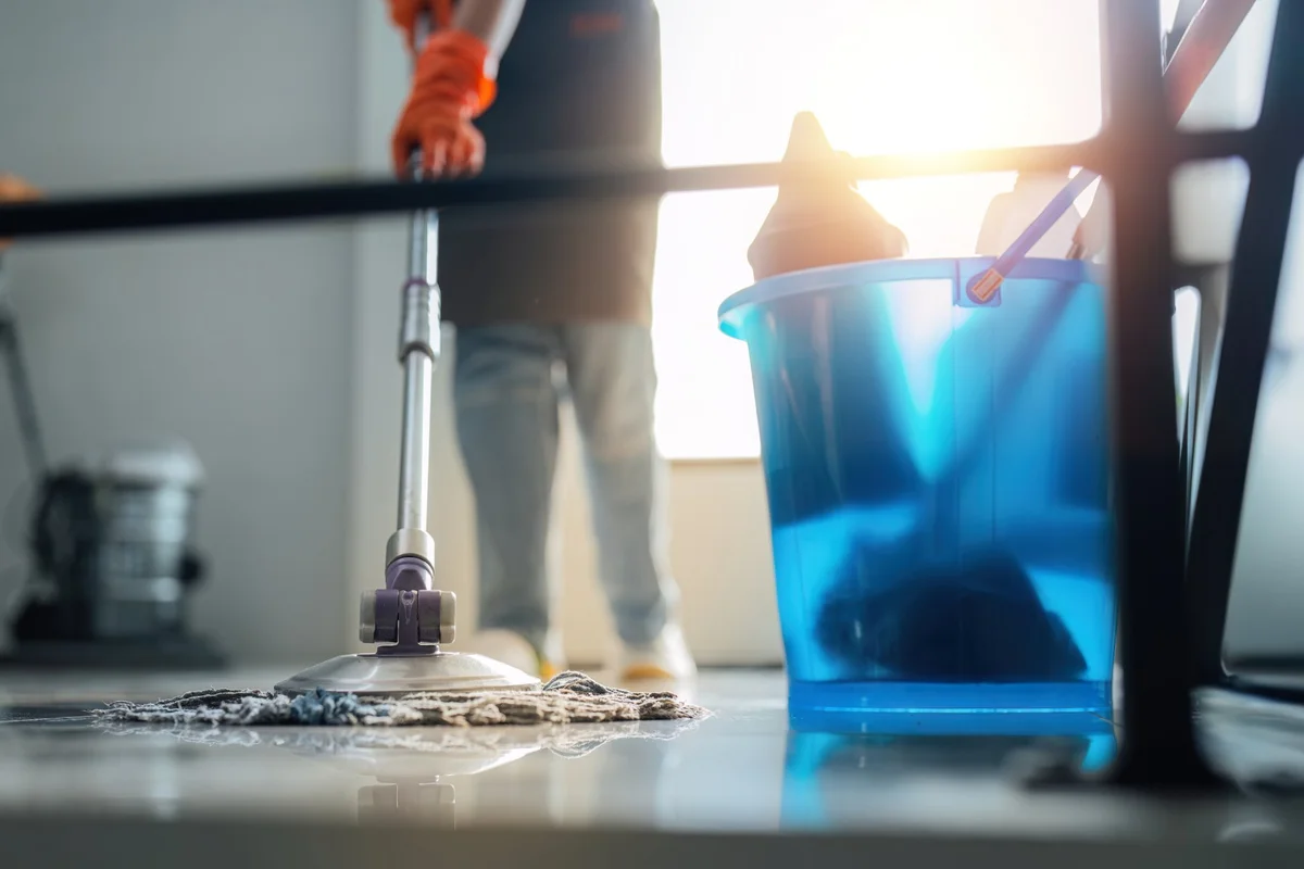 Operatore con guanti pulisce un pavimento con mop e secchio in un ambiente luminoso