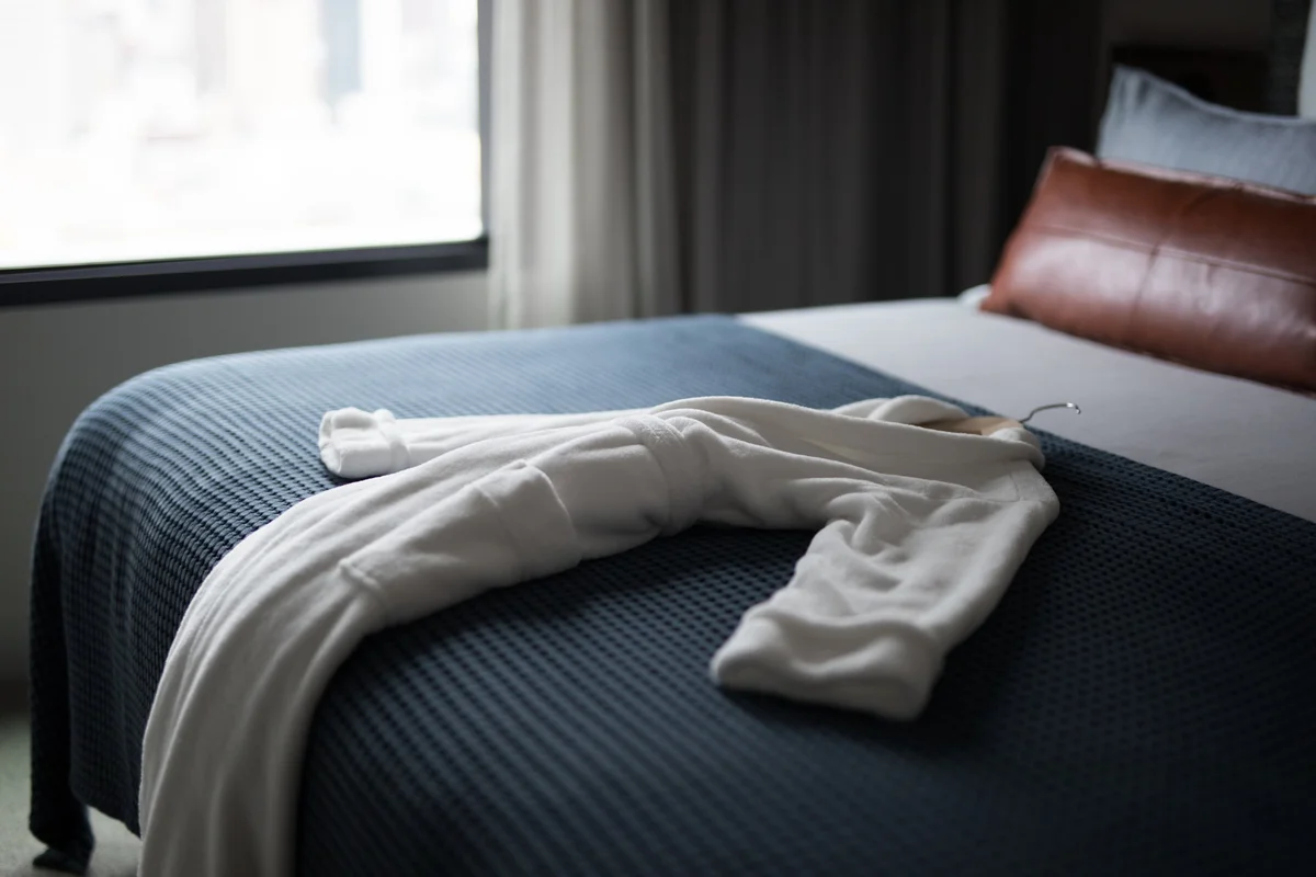 Accappatoio bianco pulito appoggiato sul letto rifatto di una camera d’hotel di lusso